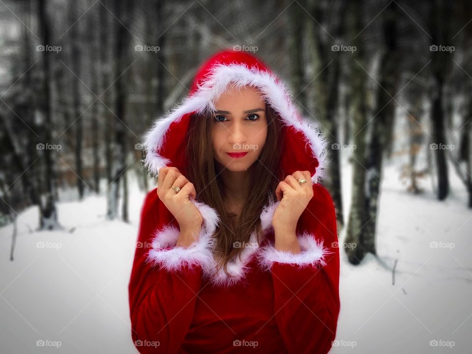 Portrait of sexy woman wearing red hood and red coat in forest of snowy trees