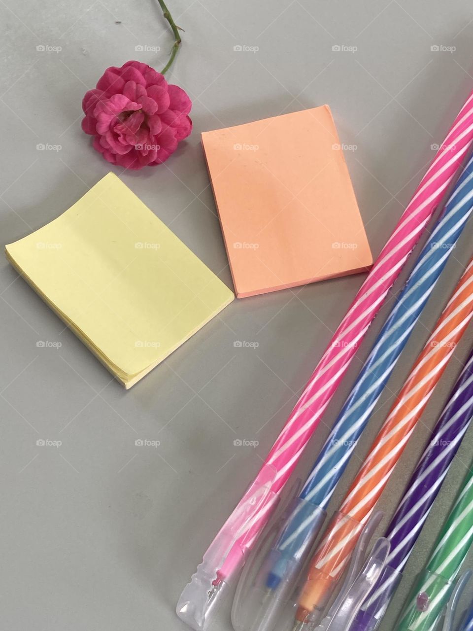 Composição com canetas coloridas, blocos de anotações e para alegrar o cenário uma pequena rosa pink.