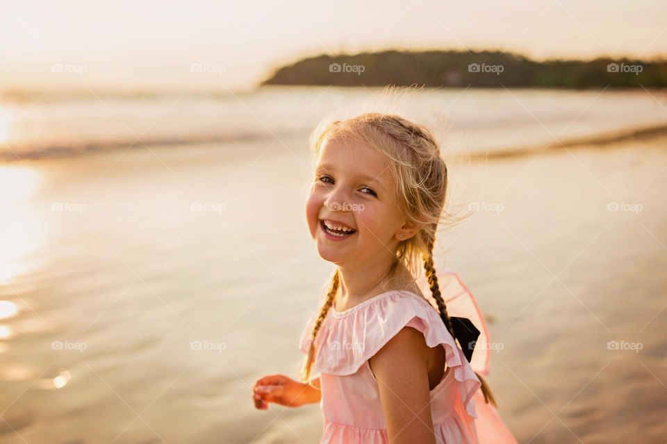 Candid lifestyle portrait of happy little Caucasian girl with blonde hair smiling on the beach 