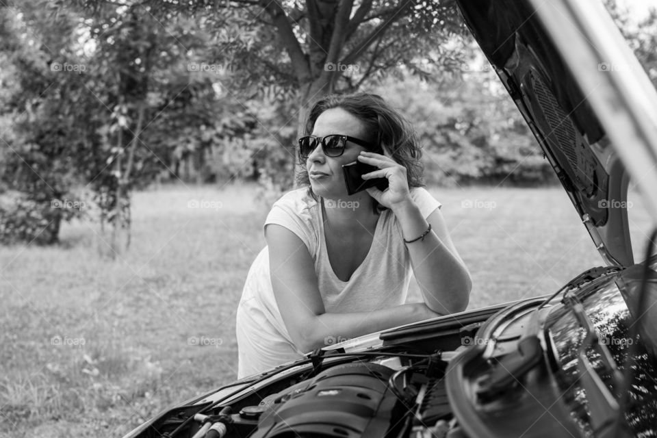 Young girl with a broken car. Young attractive girl leaning on the car and calling for road assistance