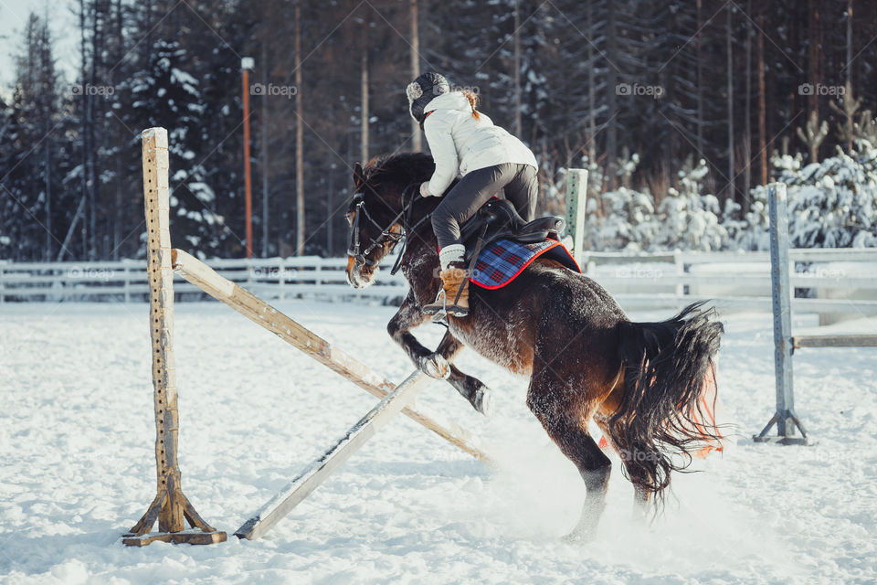 Teenage girl horseback jumping at cold winter day 