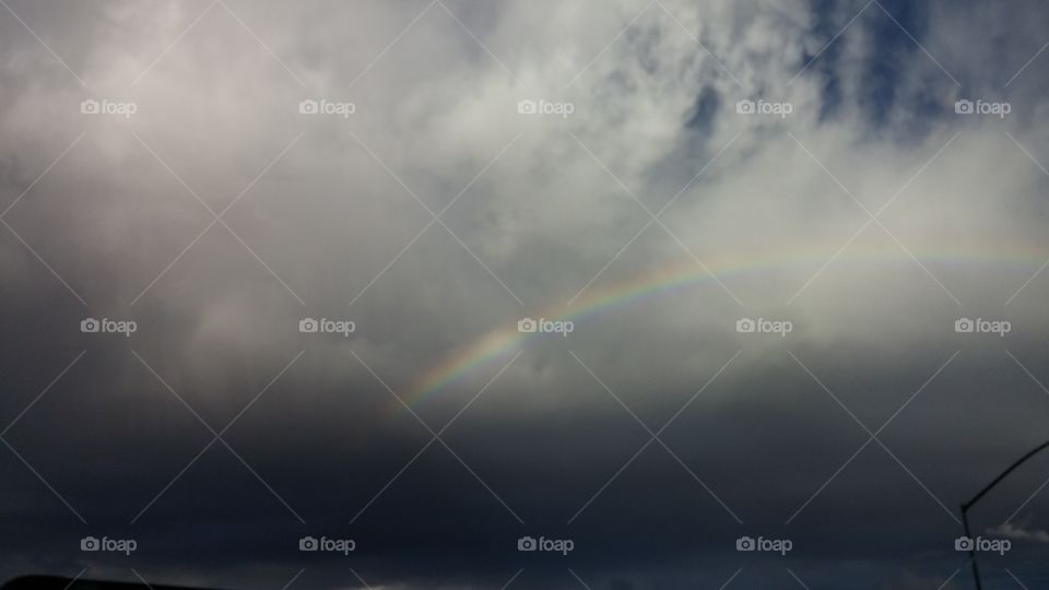 somewhere over the rainbow. a rainbow shining though the dark stormy clouds
