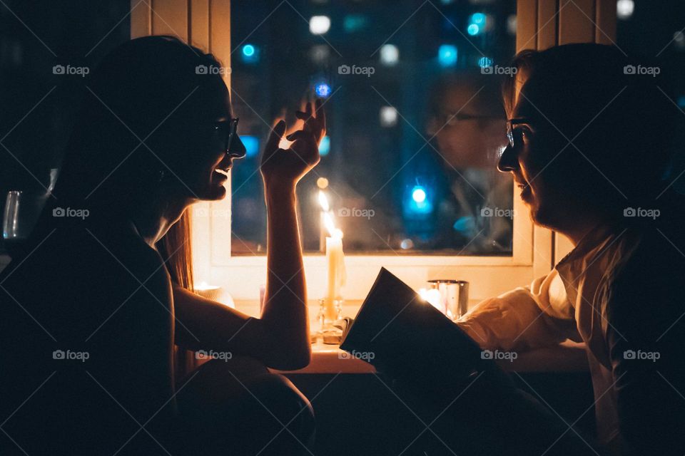 Romantic beautiful woman and man having romantic dinner by candle burning light talking to each other at Valentine’s Day. Love concept 