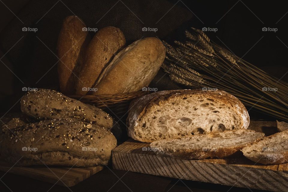 A selection of breads, displayed with wheat under subtle lighting 