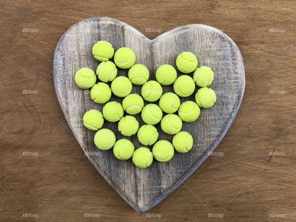Yellow tennis ball sweets on a wooden heart