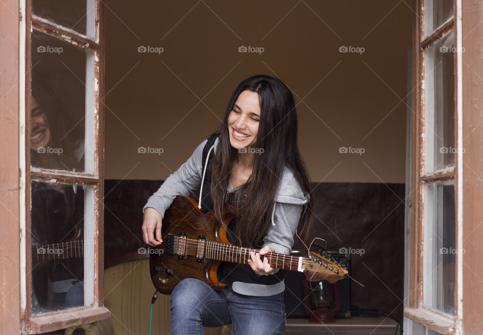 Happy beautiful woman holding guitar on the window