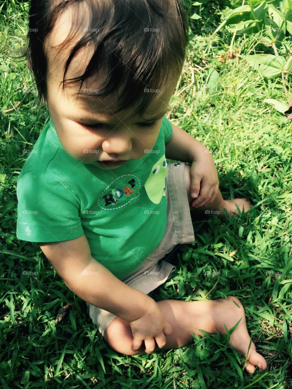Baby boy enjoying the outdoors and sitting in the grass on a summer day. 