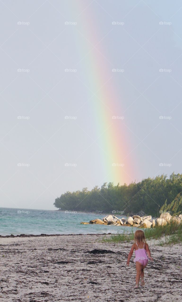 Little girl trying to find the pot of gold at the end of the rainbow while playing at the beach on a sunny day