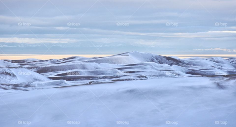 Great Sand Dunes National Park covered in snow. Very cloudy and moody shot with deep lighting. Mountains in the background 
