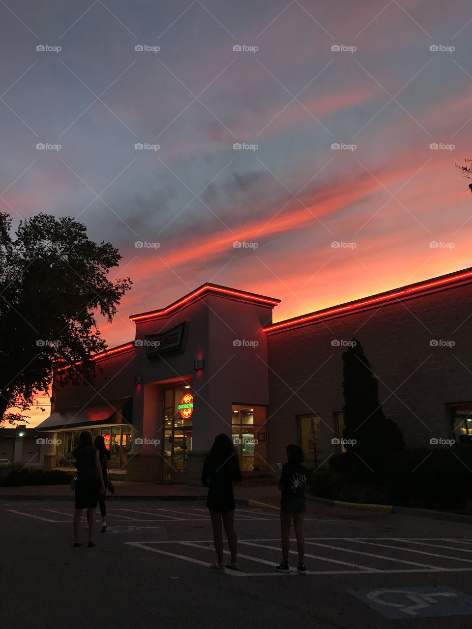 A vibrant sunset over an illuminated Krispy Kreme donut shop