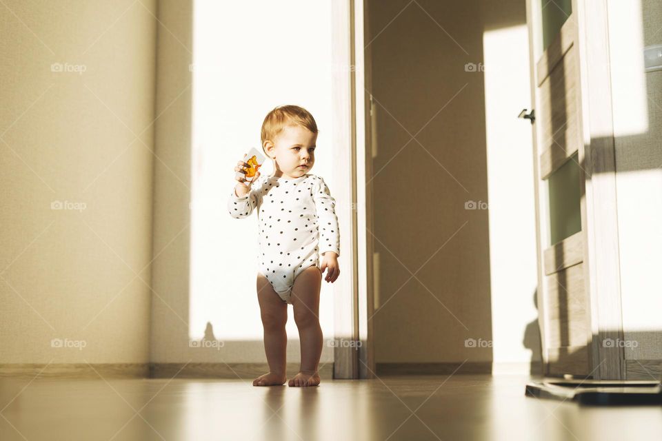 Cute baby girl in emty children room with hard light at home