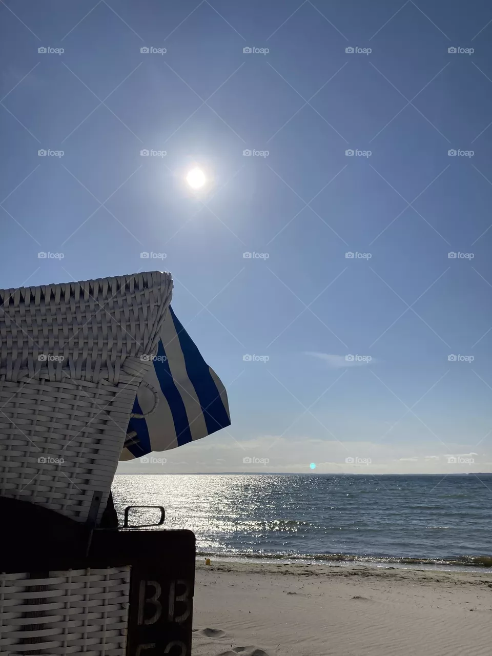Sehnsucht nach Meer.  Sonnenaufgang über der Ostsee mit blau-weißem Strandkorb in linker Bildhälfte