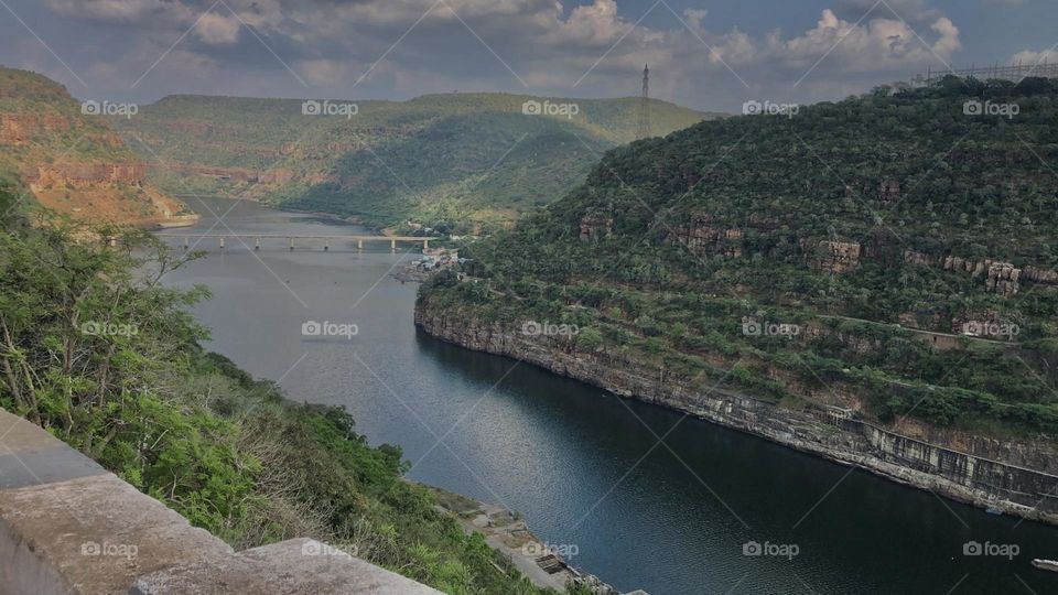 Beautiful landscape of river passing in between the green mountains and under the clouds and there’s a bridge across the river in between the mountains 🏔