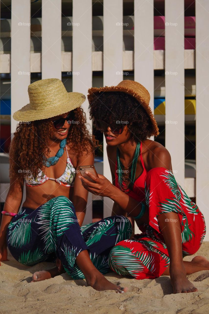 Two women sitting at the beach checking their phone 