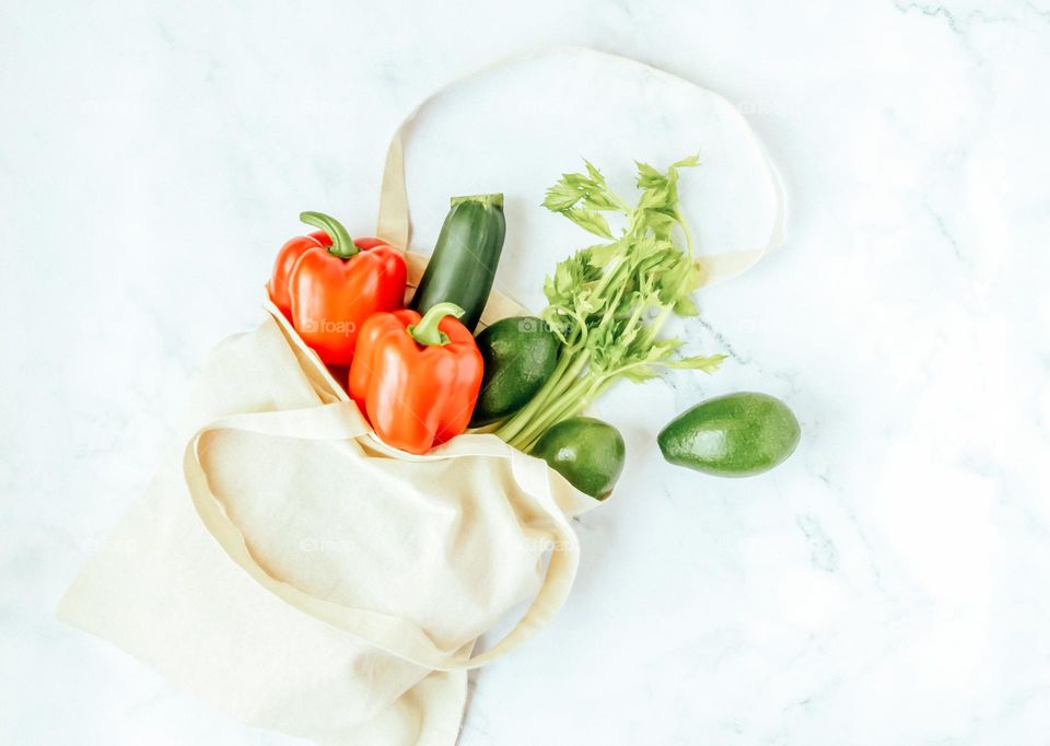 Green and red vegetables in linen reusable bag.