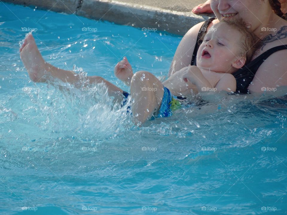 A toddler boy at the outdoor swimming pool for his first round of swimming lessons on a sunny summer evening. 