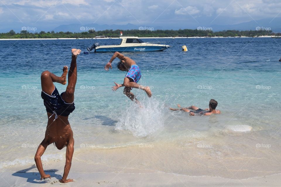 Boys active beach flips blue clear water Indonesia