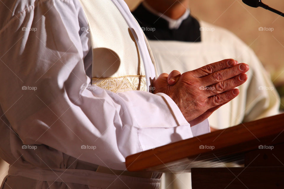 Priest holding hands together for praying in a public catholic mass