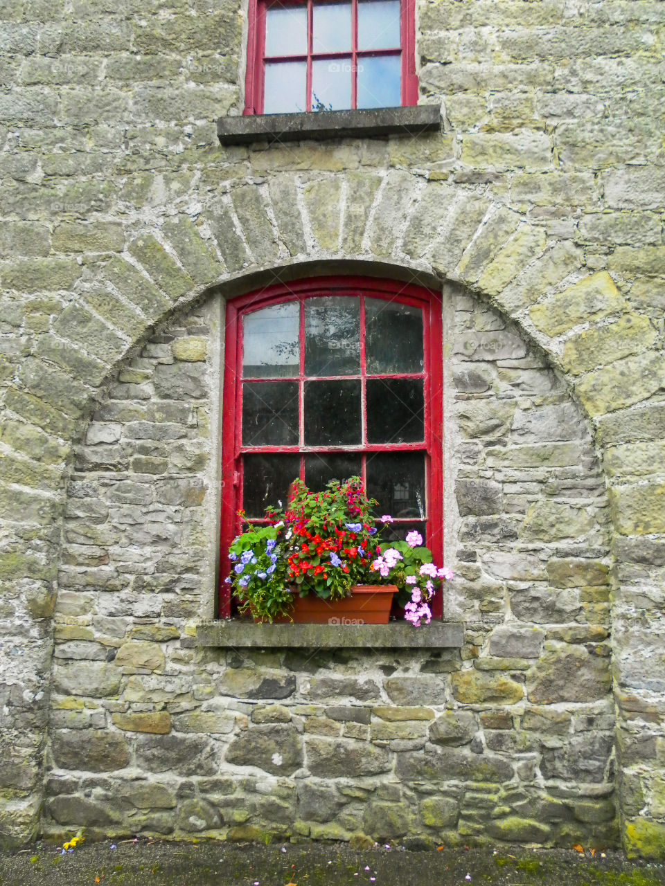 Stone wall with red window frames and flowers on the window sill. Shapes rectangles and squares in this architectural structure