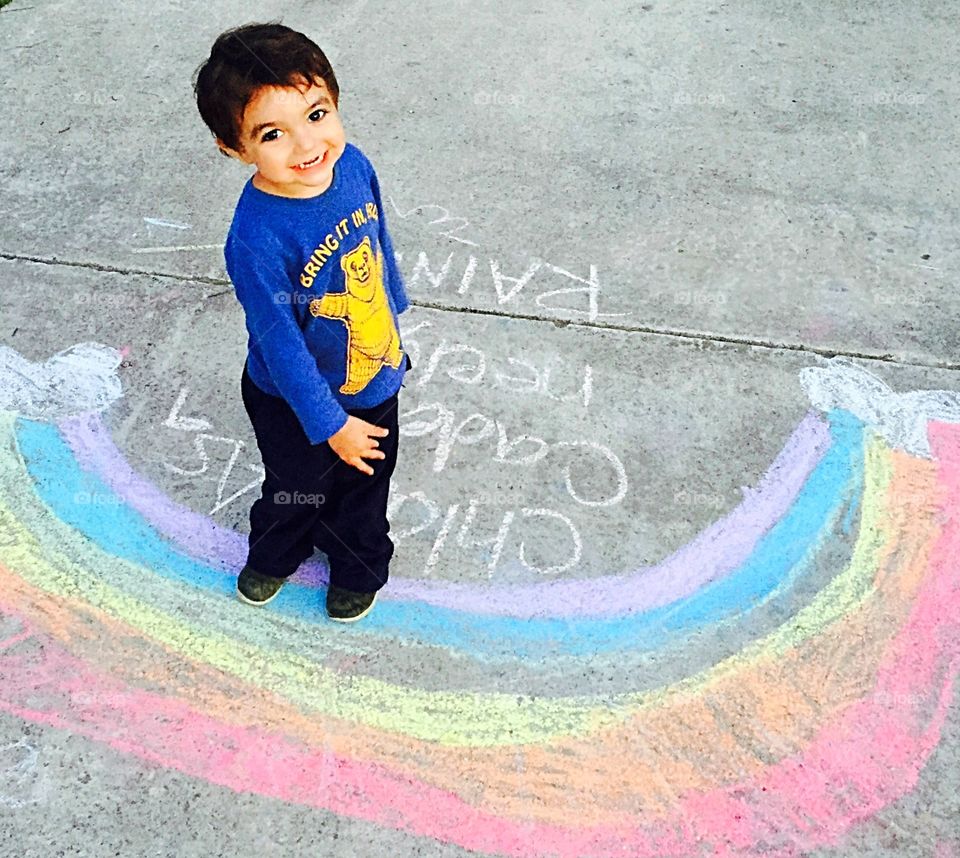 Little boy standing on his hand-drawn chalk rainbow 