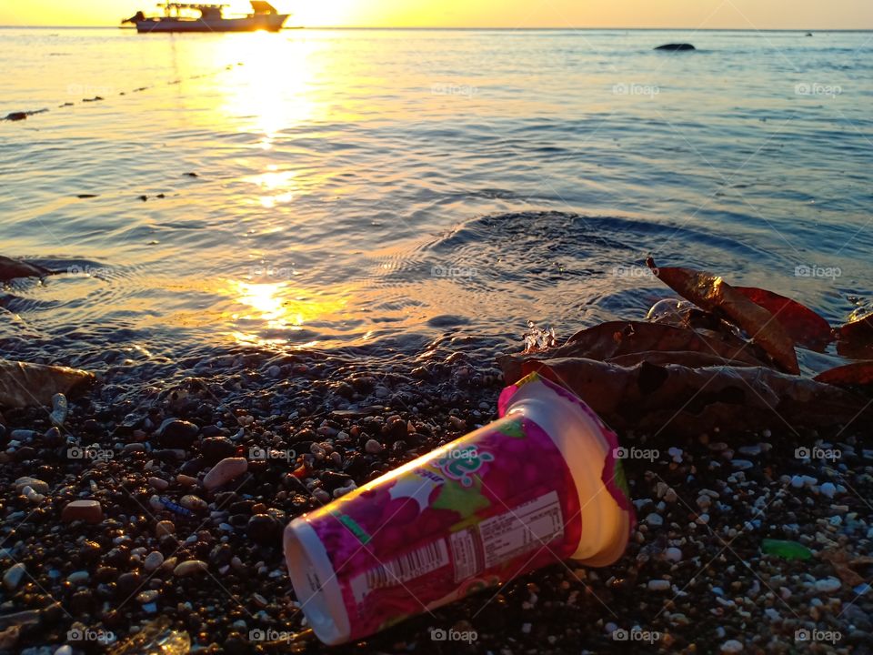abandoned plastic cup on the beach, beautiful sunset view and  fisherman boat