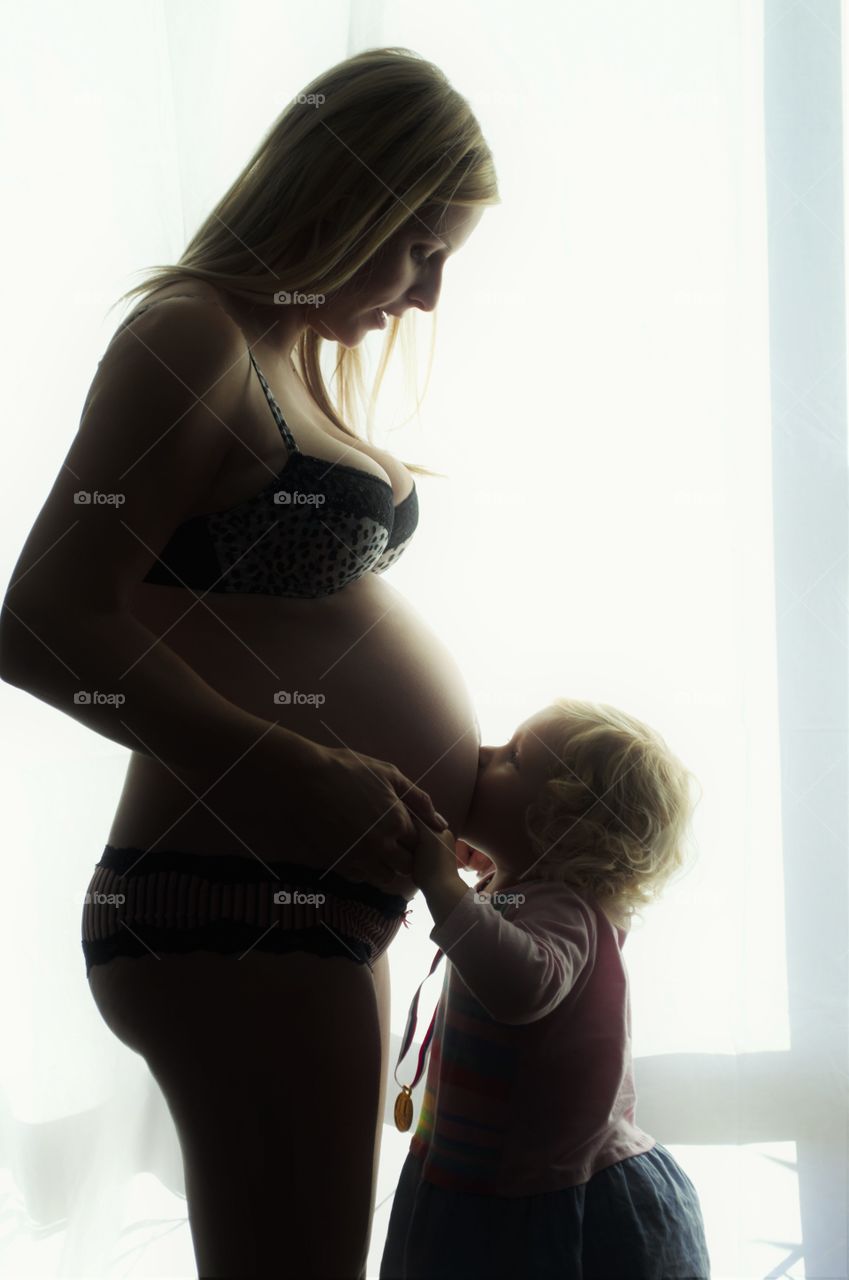 Little girl kissing her pregnant mother's tummy