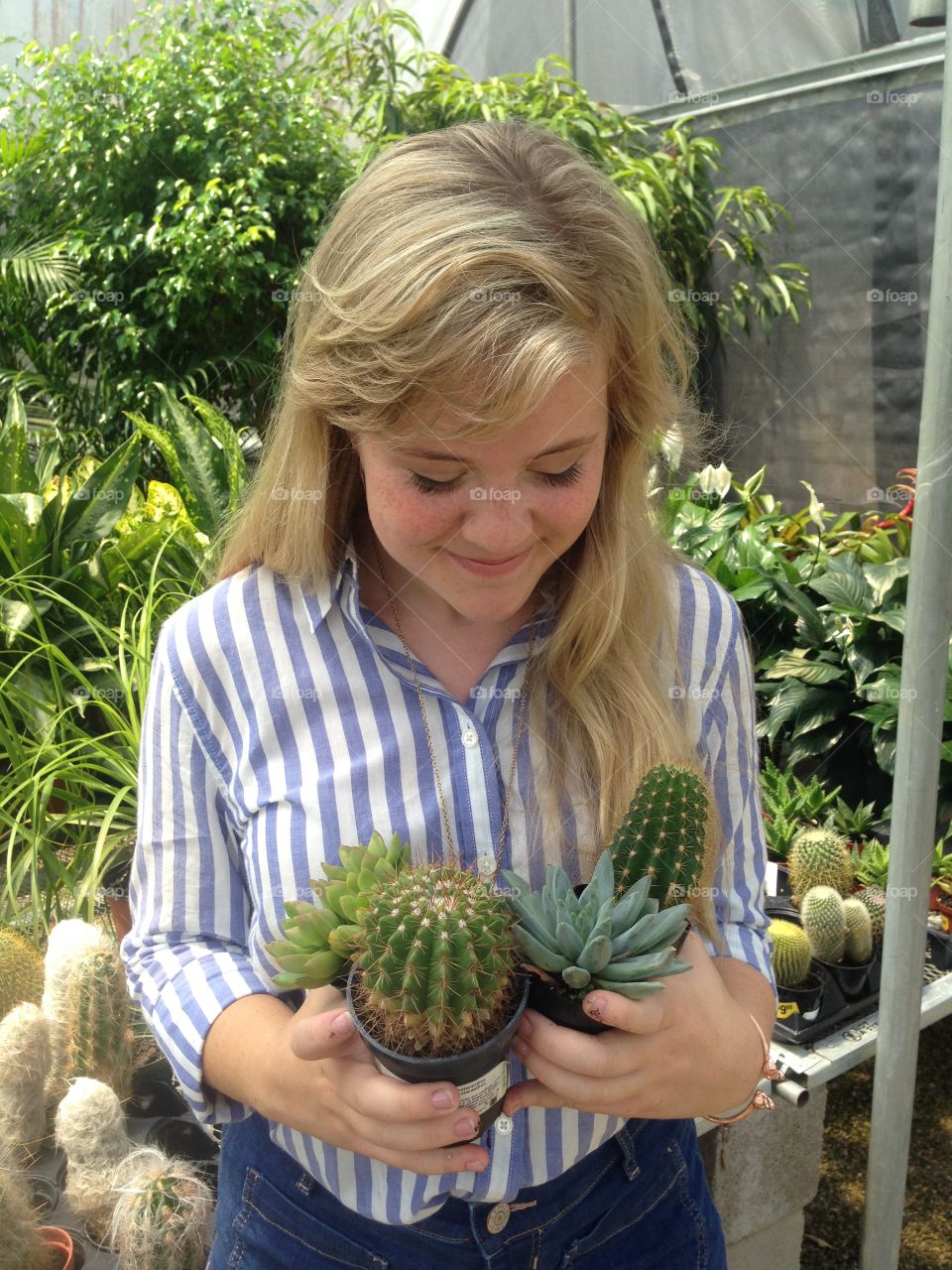 Handfuls of succulent plants, a warm greenhouse in summer. Blonde hair falling over one shoulder, a striped button-down shirt and high-waisted shorts