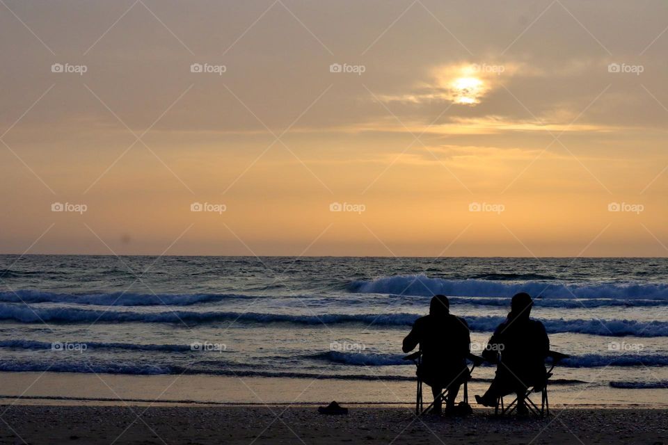 Couple sitting on the beach at sunset 