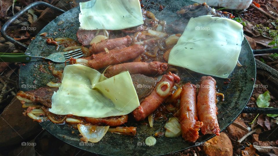 Carnes bovinas e suínas assadas no disco de grade, arado de trator, com fogo de álcool. Alcatra e linguiça com sal, tomate, cebola, pimenta, limão e queijo.