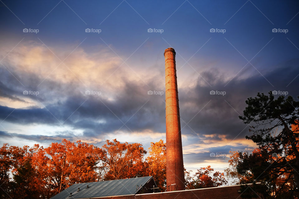 A  beautiful fall sunset brings dusk sunlight to a chimney house and highlights foliage atop trees surrounding it.