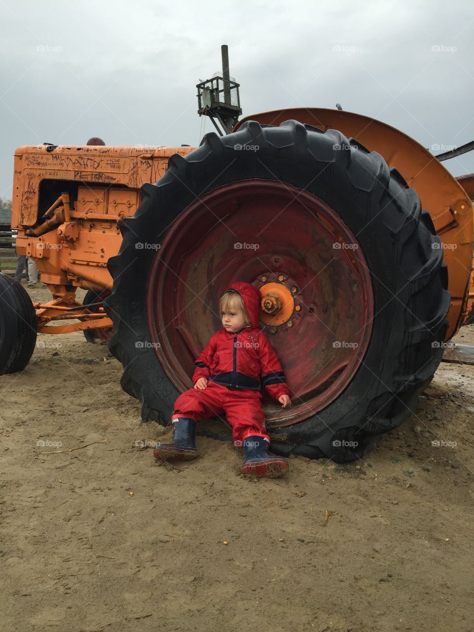 Toddler rests beside tractor wheel