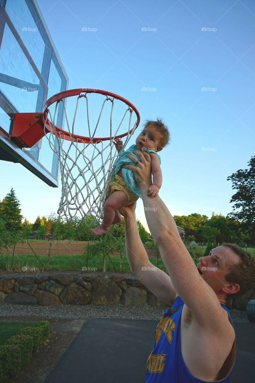 Father carrying baby to put basketball in hoop
