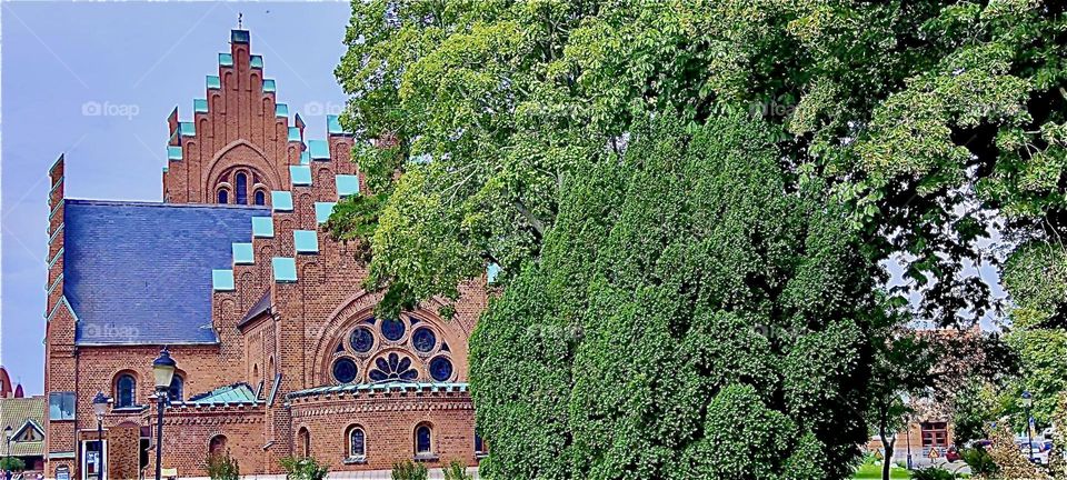 Peeking out from behind the trees is the front facade of the church in “Trelleborg” in “Sweden” by the “Baltic Sea”. 2023. Hypnotic Productions