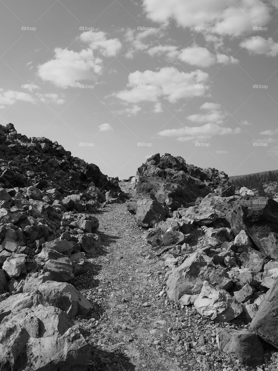 A hiking trail through the rugged terrain at the Big Obsidian Flow in the Newberry National Volcanic Monument in Central Oregon on a sunny fall day with fluffy clouds in the sky. 