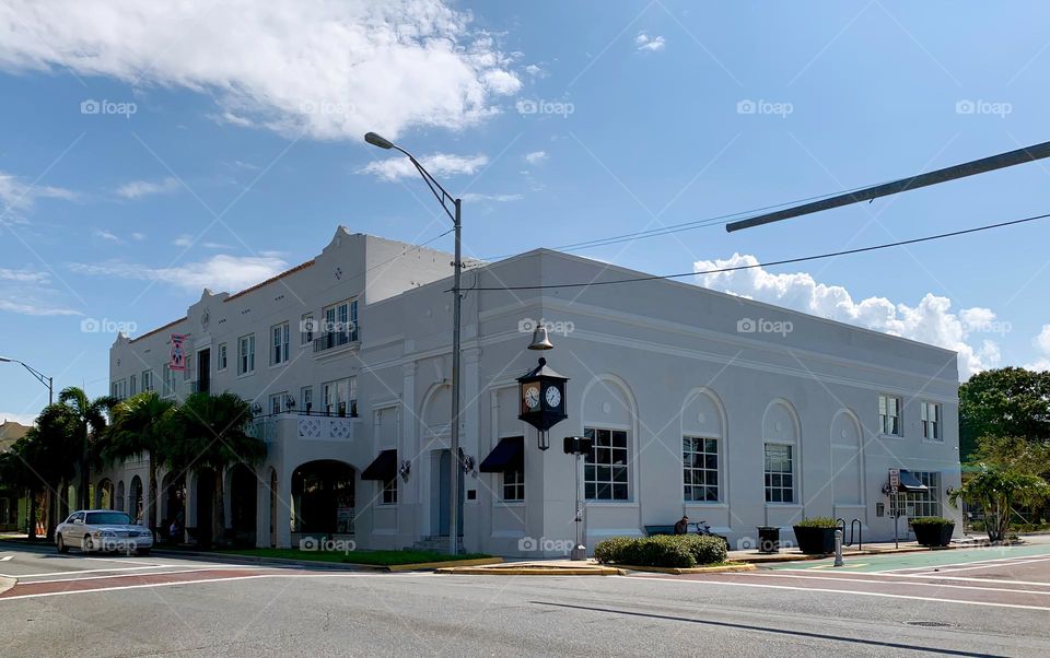 Architectural historical commercial building with rounded top arched openings with palm trees in front of the facade with three stories levels and multiple grilles windows and old clock on the street corner.