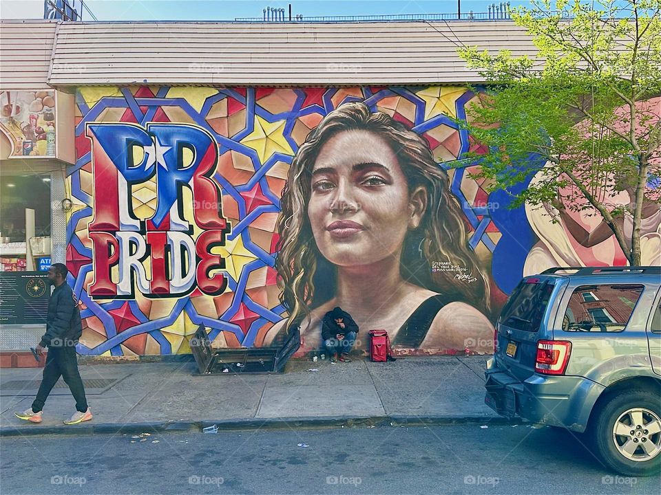 Latin “PRIDE” is celebrated here in this large artful mural with pop art patterns, a young Hispanic woman and stars on “Jefferson Street” off “Broadway” in “Bushwick”, Brooklyn. It extends over nearly an entire city block. 2024. Hypnotic Productions