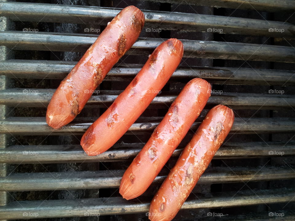 Four hot dogs cooking on the grill