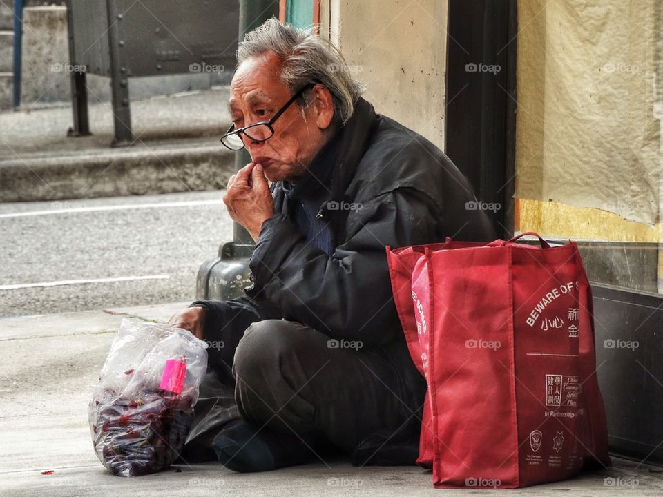Old Homeless Man Sitting On The Sidewalk. Homeless In America
