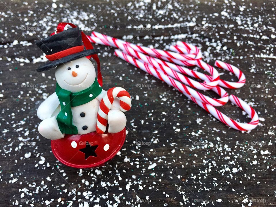 Tiny snowman for hanging in the Christmas tree with candy canes on wooden table powdered with snow