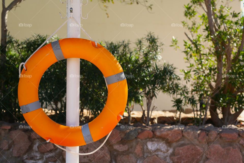 a round lifebuoy hangs on a white stand near the pool