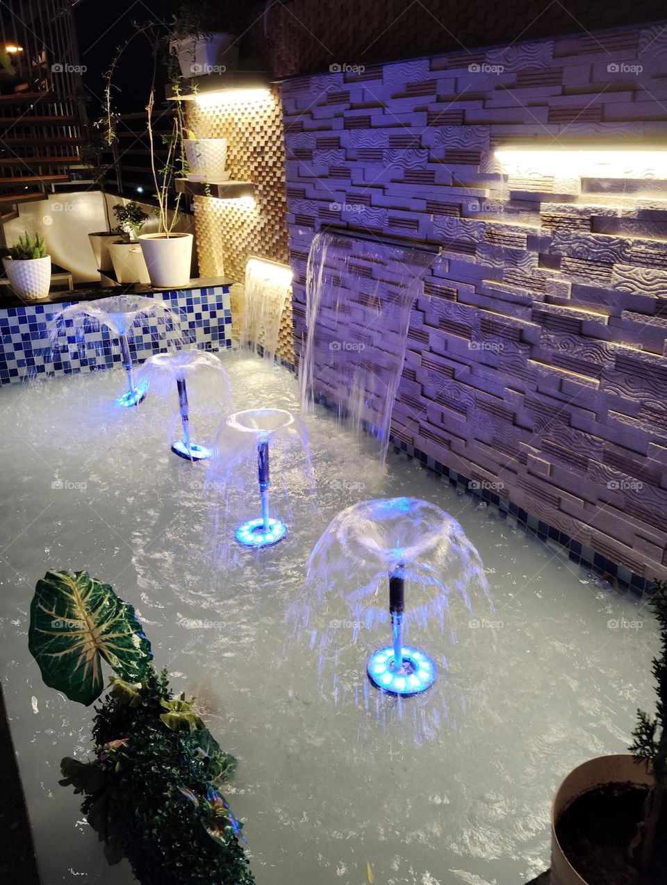 the fountain showing water with blue color, night scene, yellow light green plant all looks very beautiful