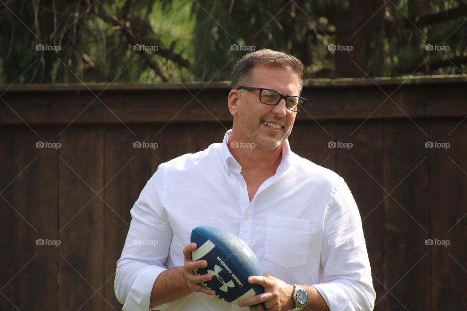 Man with short beard smiling outdoors on sunny day holding football