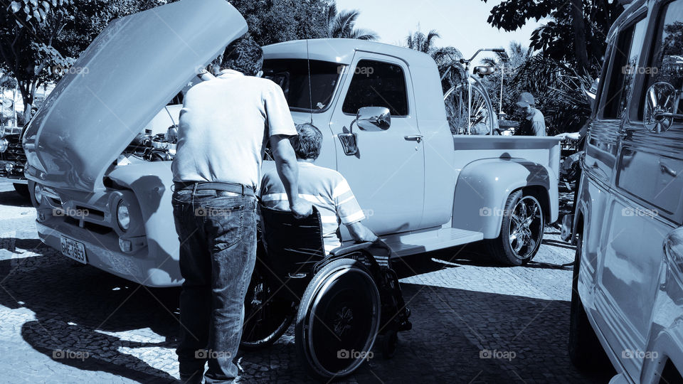 Homem conduzido outro em cadeira de rodas.