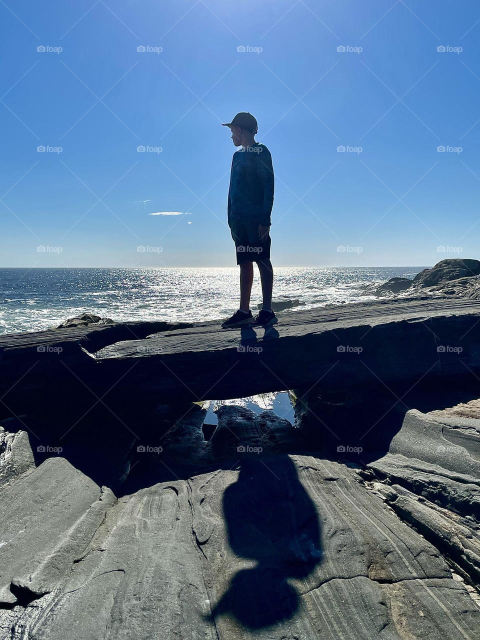 A Teenager Stands On A Sliver Of Granite As The Sun Both Silhouettes And Casts The Figure’s Shadow.