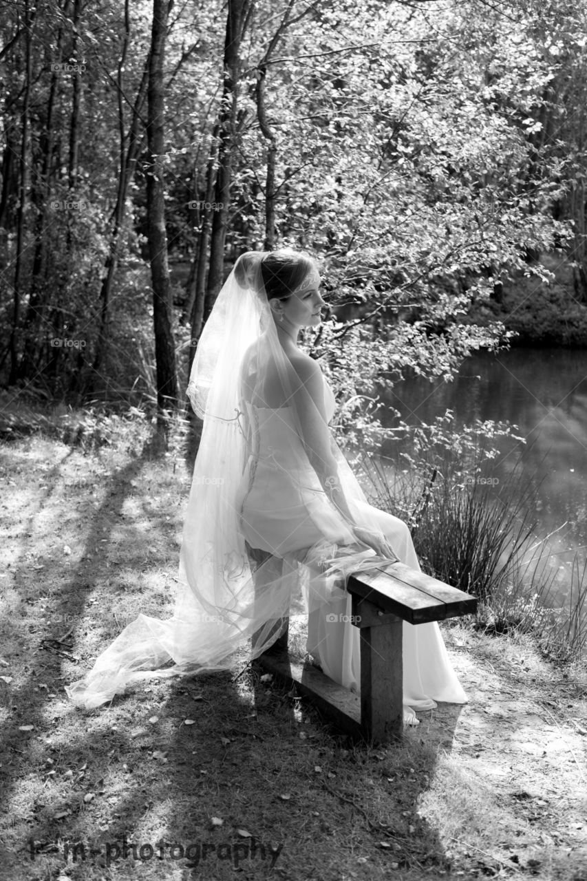 Beautiful bride sitting on bench in forest