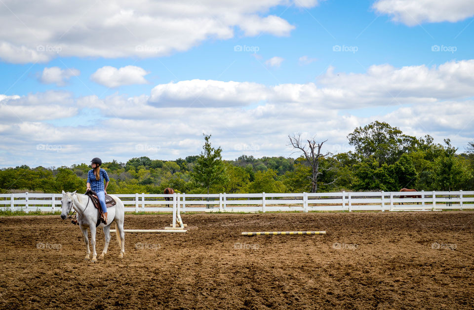 Woman on a horse in a jumping field with trees and sky in the background