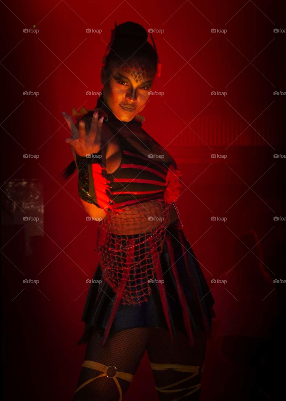 beautiful voodoo zombie go-go dancer in a deep orange red light looking at the camera and luring you to come closer