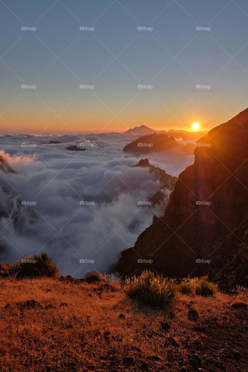A stunning sunset is captured at the top of the mountains. The golden sun is slowly descending towards the horizon, casting a warm gold over the entire scene. 