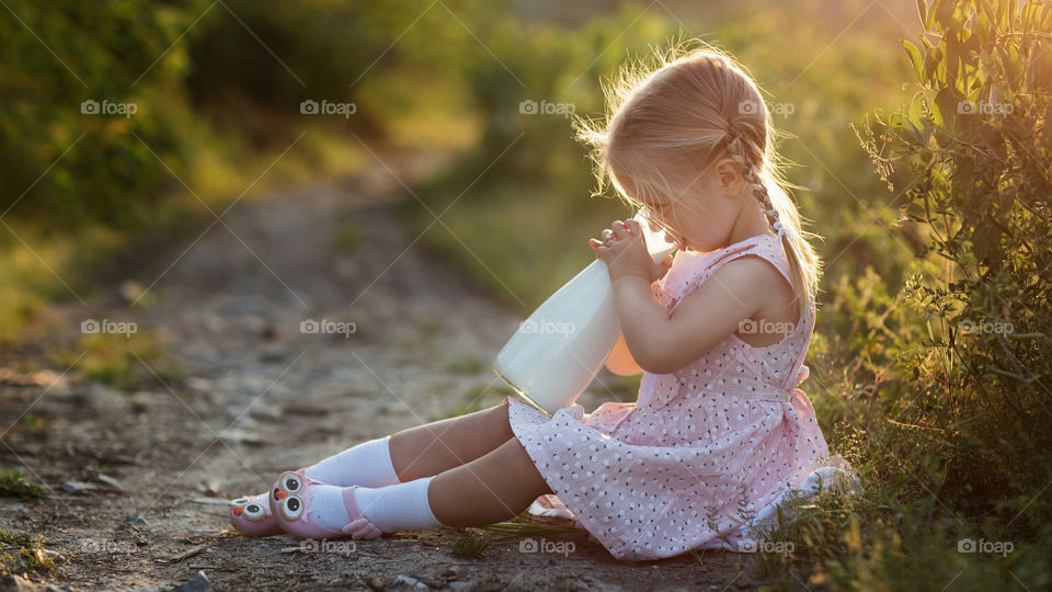 Cute little girl with blonde hair drinking milk in village 