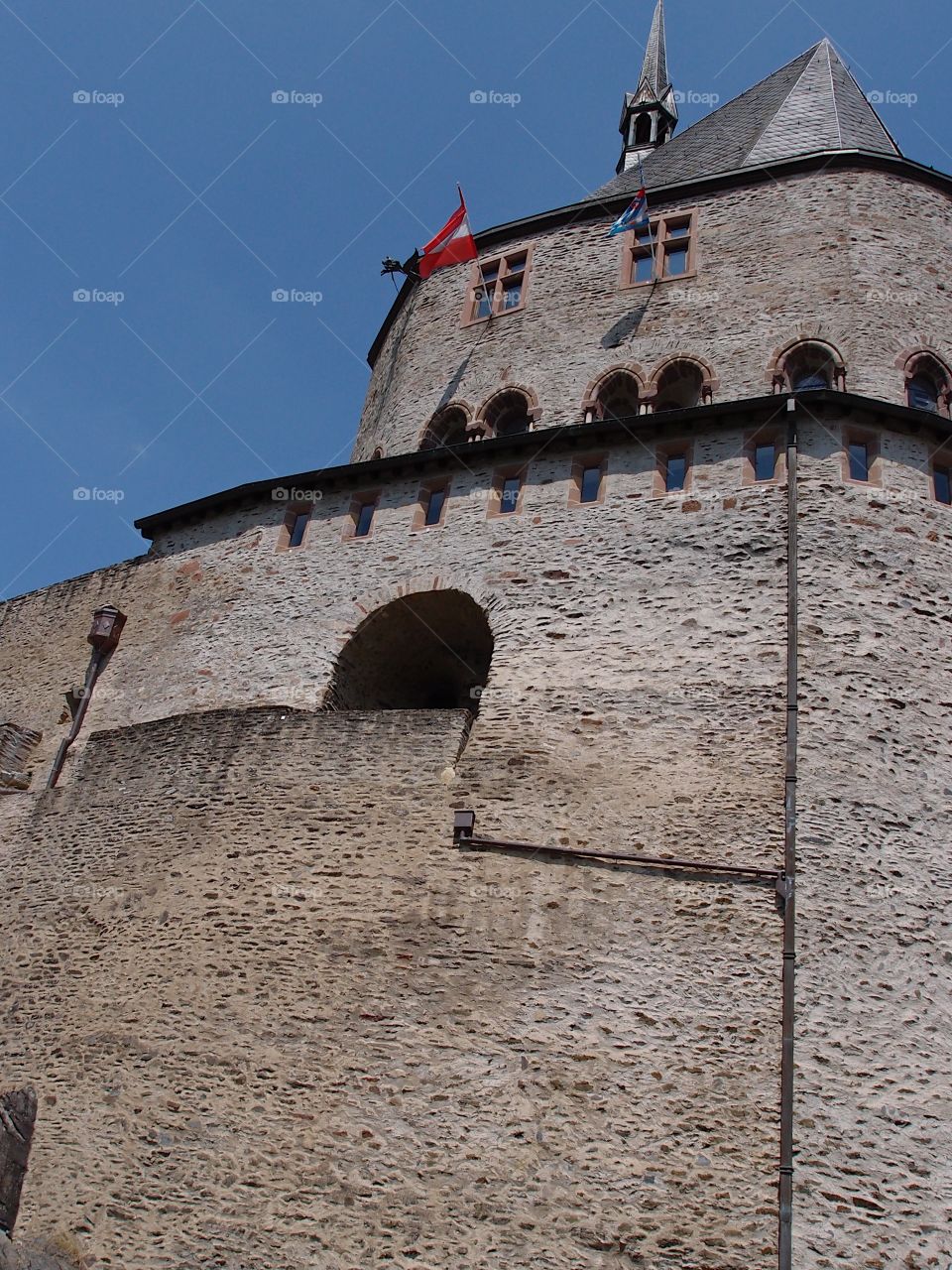 The exterior wall of Chateau dé Vianden in Luxembourg made of layers of stone and designed with arches on a sunny summer day. 